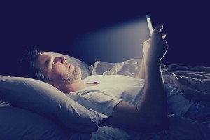 Man laying in dark on bed looking at light from phone